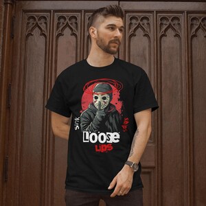 Op de afbeelding: Zwart T-shirt met een afbeelding van een gemaskerd figuur op een rode achtergrond en de tekst "Sink ships Loose Lips".