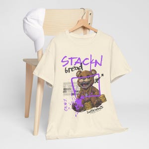 Stackin Bread Teddy Graphic T-Shirt in Natural Color is your go-to for trendy streetwear. Featuring bold graphics and a soft, wearable design, this unisex tee is perfect for casual outfits or unique gifts. A must-have for urban style lovers.