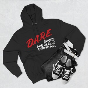 May include: Black hooded sweatshirt with the text "D.A.R.E. DRUGS ARE REALLY EXPENSIVE" in red and white. The sweatshirt is paired with dark denim jeans, a white belt, and black and white sneakers.
