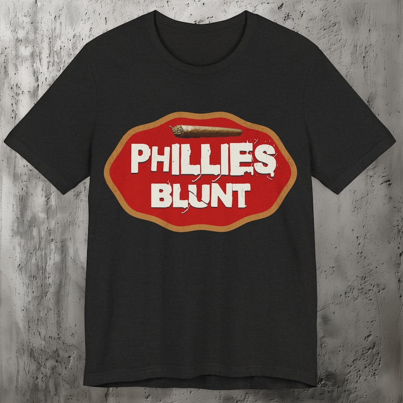 Op de afbeelding: Zwart T-shirt met een rode en gouden afbeelding van een sigaar met de tekst "PHILLIES BLUNT".