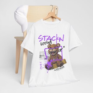 Step up your streetwear game with the Stackin' Bread Teddy Graphic T-Shirt in White. Featuring a bold teddy bear design, this shirt offers stylish comfort for men and women. A versatile tee perfect for casual wear or urban-inspired outfits.