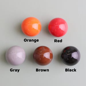 May include: Five glossy, spherical objects in orange, red, grey, brown, and black. Each sphere has a reflective surface. The colours are labelled with the corresponding colour names: Orange, Red, Gray, Brown, and Black.
