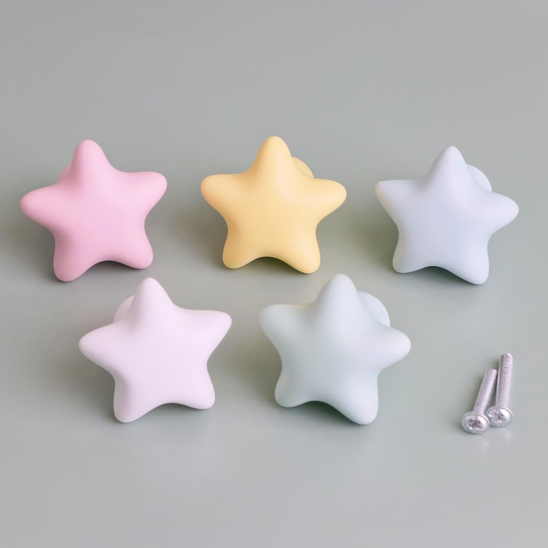 Op de afbeelding: Vijf stervormige kastknoppen in pastelkleuren: roze, geel en blauw. De knoppen zijn gemaakt van een glad materiaal en bevatten twee zilveren schroeven voor de installatie. Deze decoratieve knoppen zijn ideaal voor kindermeubels.