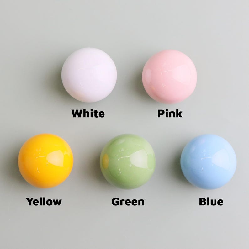 May include: Five glossy, round knobs in white, pink, yellow, green, and blue. Each knob is labelled with its colour name in a bold, black font. The knobs are arranged on a light grey background.