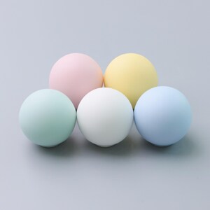 May include: Five pastel-colored spheres arranged on a gray surface. The spheres are in shades of pink, yellow, white, blue, and green. The smooth, round objects are evenly spaced and appear to be made of a matte material.