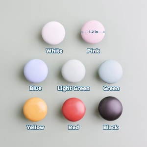 Op de afbeelding: Een verzameling van acht ronde kastknoppen in verschillende kleuren: wit, roze, blauw, lichtgroen, groen, geel, rood en zwart. Elke knop heeft een diameter van ongeveer 3 cm.