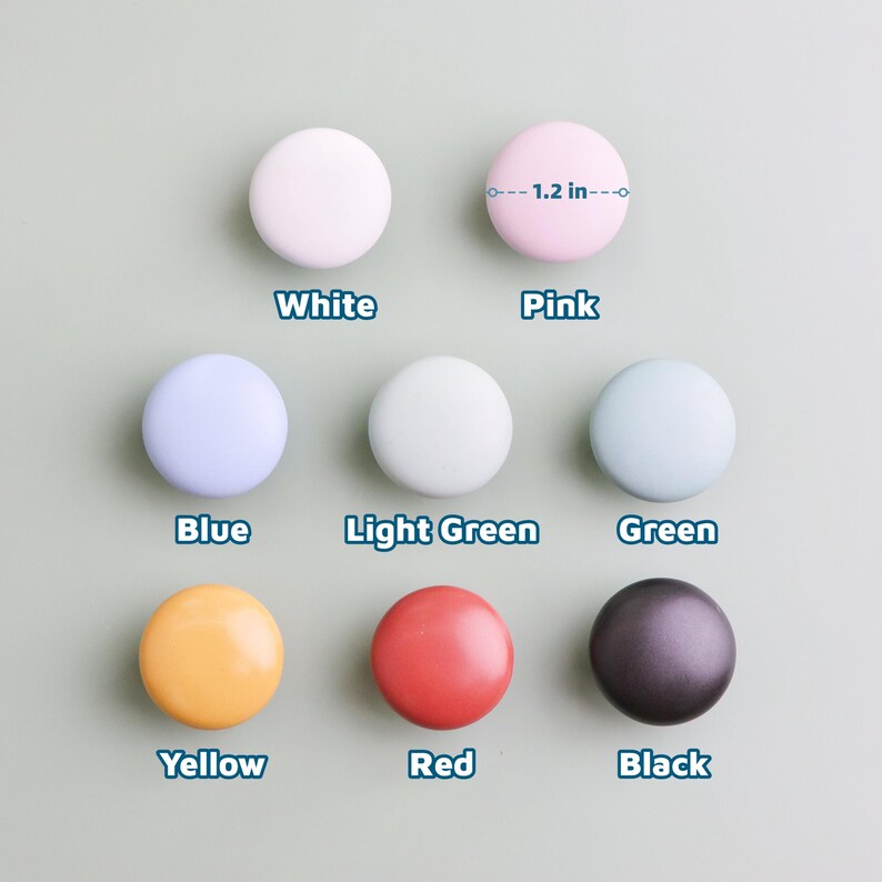 Op de afbeelding: Een verzameling van acht ronde kastknoppen in verschillende kleuren: wit, roze, blauw, lichtgroen, groen, geel, rood en zwart. Elke knop heeft een diameter van ongeveer 3 cm.