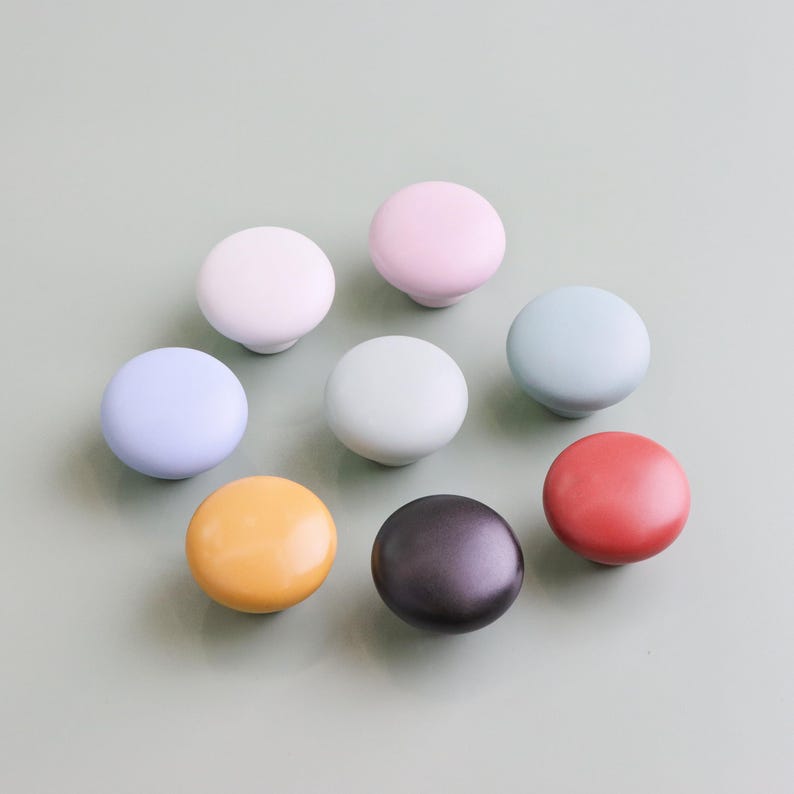 Op de afbeelding: Een verzameling van acht kleurrijke keramische kastknoppen in verschillende pastel- en felle kleuren, waaronder wit, roze, blauw, groen, geel, zwart en rood. De knoppen zijn rond en hebben een gladde, glanzende afwerking. Diameter ongeveer 3 cm.