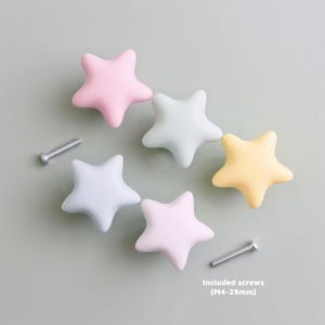 Op de afbeelding: Vijf stervormige kastknoppen in pastelkleuren: roze, lichtblauw, geel en mintgroen. Twee zilveren schroeven zijn inbegrepen. De knoppen zijn gemaakt van een glad materiaal. Ideaal voor kindermeubels of een grillig decoratiethema.