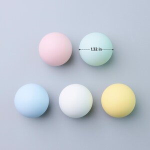 May include: Five pastel-colored spheres, each approximately 1.32 inches in diameter, are arranged on a gray surface. The spheres are in shades of pink, light green, blue, white, and yellow. The image is a top-down view.
