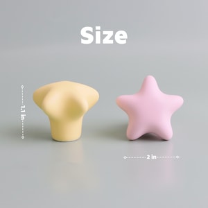 Op de afbeelding: Twee decoratieve kastknoppen. E&eacute;n is geel en bloemvormig, meet 2,8 cm. De andere is roze en stervormig, meet 5,1 cm. Het woord "Size" staat boven de knoppen.