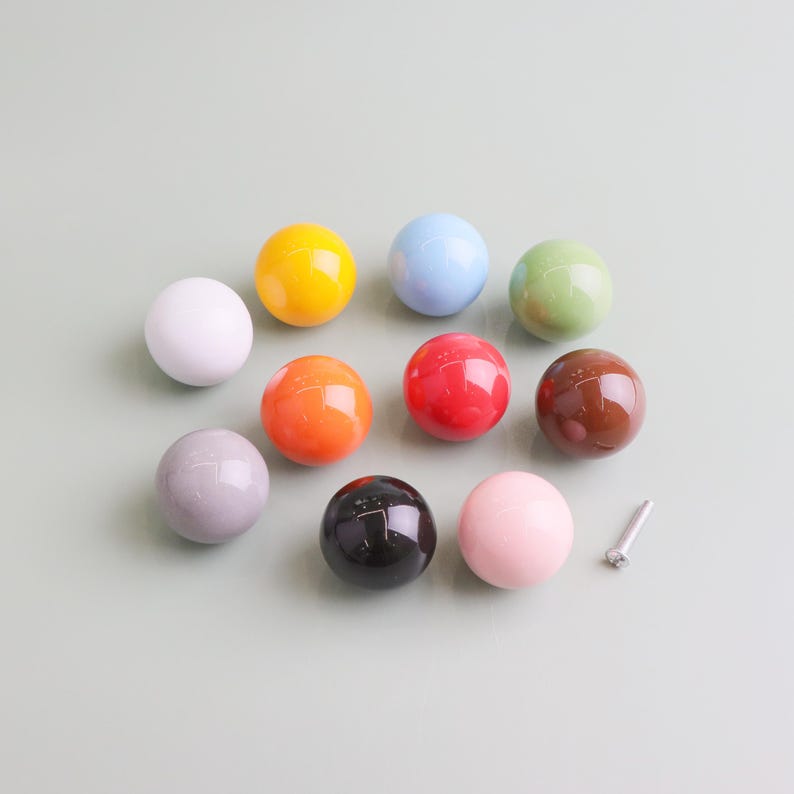 May include: Nine spherical cabinet knobs in a range of colours: white, yellow, blue, green, red, brown, grey, black, and pink. A silver screw is also visible. These knobs are likely for furniture or decorative use.