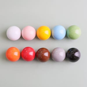 May include: Ten glossy, spherical knobs in a range of colours: white, pink, yellow, blue, green, orange, red, brown, grey, and black. The knobs are arranged in two rows of five.