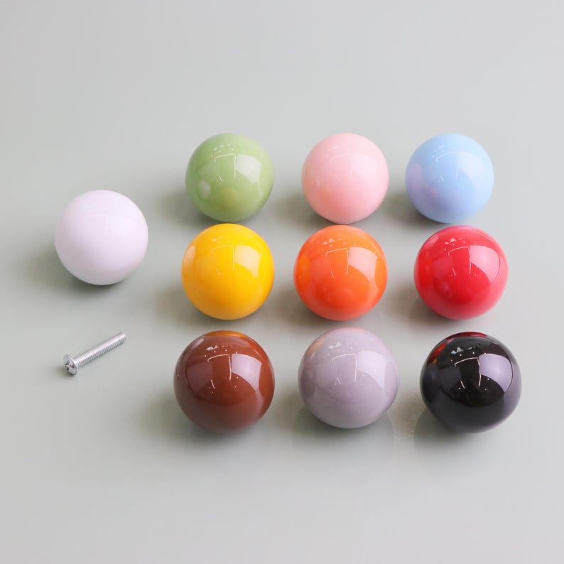 May include: A selection of glossy, spherical cabinet knobs in a range of colours: white, green, pink, blue, yellow, orange, red, brown, grey, and black. A silver screw is also visible.