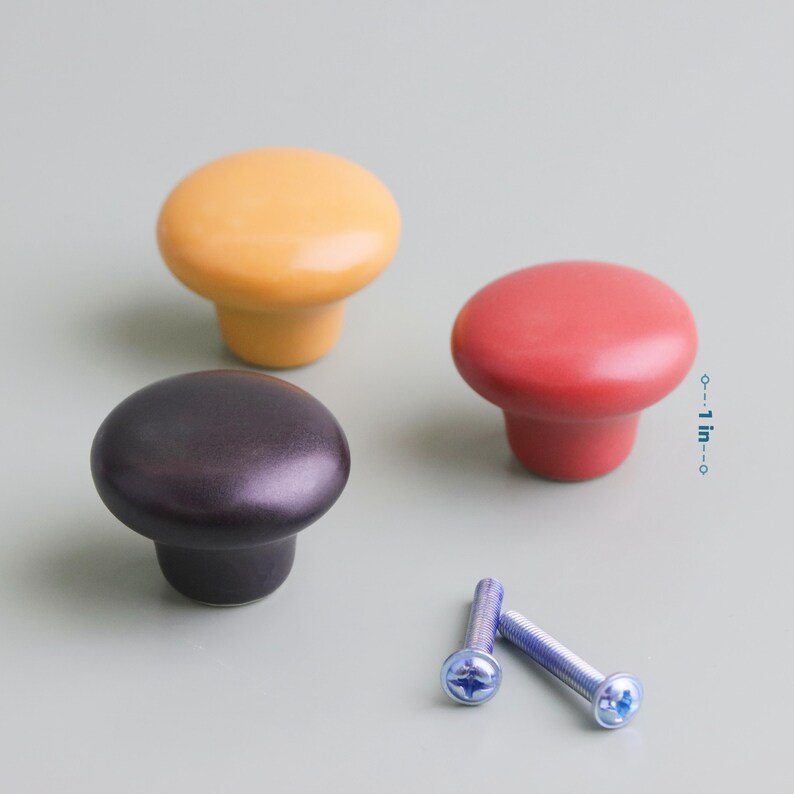 Op de afbeelding: Drie kleurrijke kastknoppen in geel, rood en donkerpaars, met twee schroeven. De knoppen hebben een diameter van ongeveer 2,5 cm. Deze decoratieve knoppen zijn perfect om een vleugje kleur aan meubels toe te voegen.