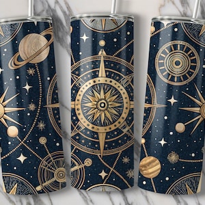 Op de afbeelding: Drie roestvrijstalen bekers met een donkerblauwe achtergrond en gouden hemelse ontwerpen. De ontwerpen omvatten sterren, planeten en een kompasroos.