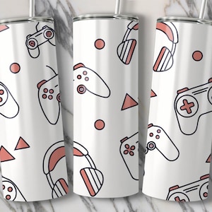 May include: White tumbler with a repeating pattern of video game controllers, headphones, circles, and triangles in black and coral. The tumbler has a silver rim and a clear straw.