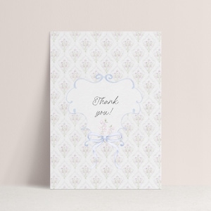 May include: A thank you card with a floral pattern background. The card features a light blue frame with the words "Thank you!" in elegant script. A light blue bow and floral accents complete the design.