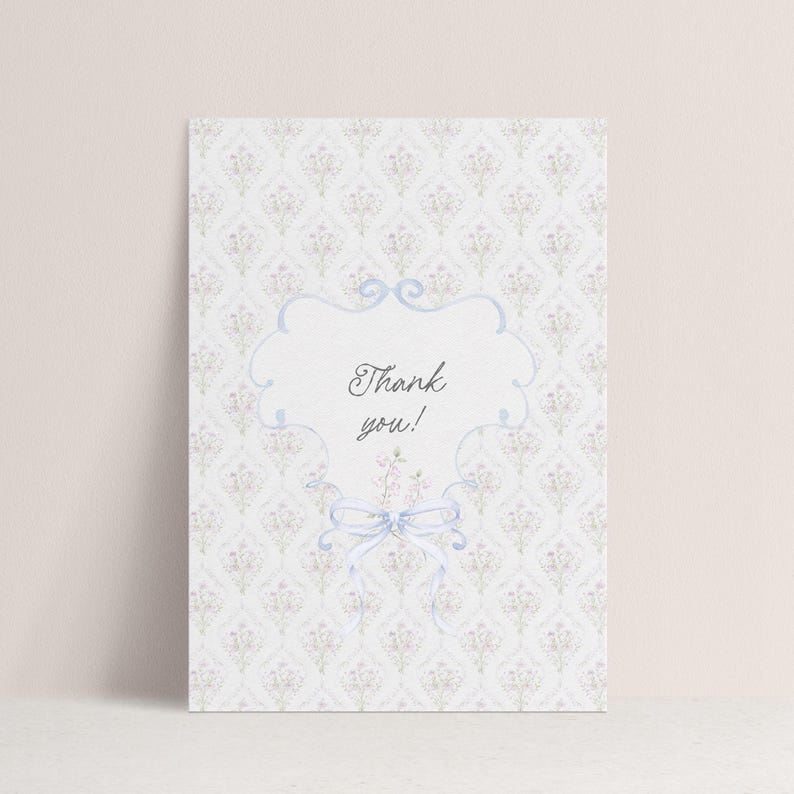 May include: A thank you card with a floral pattern background. The card features a light blue frame with the words "Thank you!" in elegant script. A light blue bow and floral accents complete the design.