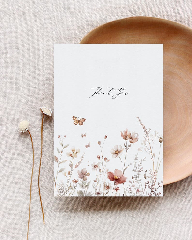 Puede incluir: Una tarjeta blanca con el texto "Gracias" en caligraf&iacute;a negra. La tarjeta presenta una ilustraci&oacute;n de acuarela de un campo de flores silvestres y mariposas en tonos marrones, rosas y verdes.