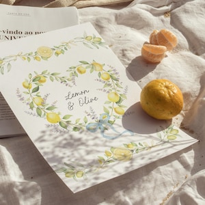 May include: A watercolor print featuring a heart-shaped wreath of lemons and olive branches, with the text "Lemon & Olive". A blue ribbon accents the design. A whole lemon and tangerine segments are next to the print.