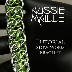 Pode incluir: Um bracelete de malha de corrente verde e prateado, conhecido como bracelete de minhoca lenta, é mostrado em um fundo preto. O texto "Aussie Maille Tutorial Slow Worm Bracelet" é exibido abaixo do bracelete.