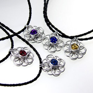 May include: Four silver chainmaille flower pendants with different colored centers. The pendants are on black cords.