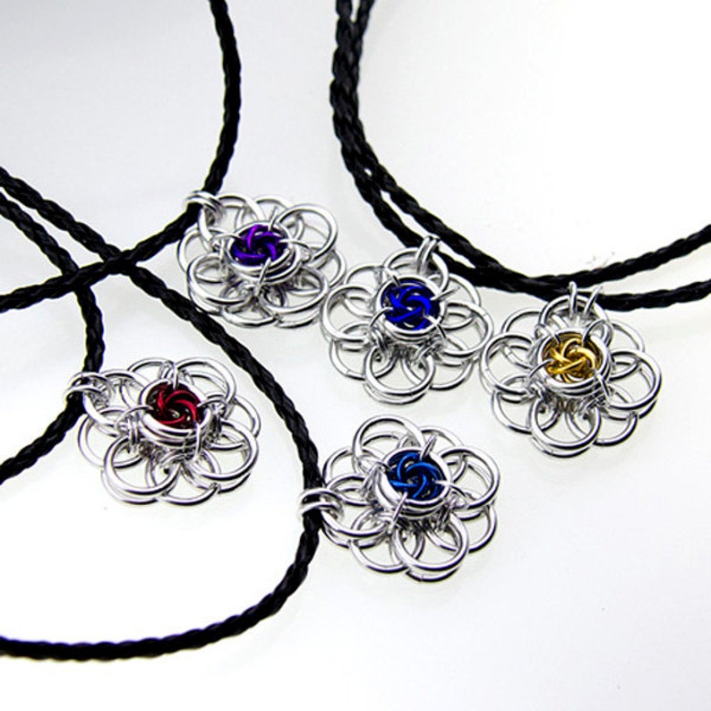 May include: Four silver chainmaille flower pendants with different colored centers. The pendants are on black cords.