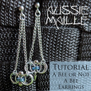 May include: Silver chainmail earrings with a bee-themed design. The earrings feature multiple silver rings, blue accents, and a small, pointed charm. The image includes the text "Aussie Maille" and "Tutorial A Bee or Not A Bee Earrings."