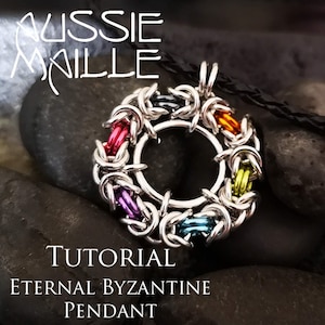 May include: A silver chainmail pendant with a circular design. The pendant is made with silver rings and features a rainbow of colors, including red, orange, yellow, green, blue, and purple. The pendant is on a black cord and is resting on a bed of gray rocks. The text "TUTORIAL" and "ETERNAL BYZANTINE PENDANT" is below the pendant.