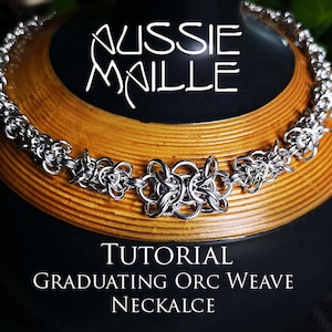 May include: A silver chainmail necklace with a woven design. The necklace is on a wooden surface and the text "TUTORIAL GRADUATING ORC WEAVE NECKALCE" is below the necklace.