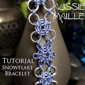 May include: A close-up of a silver and blue chainmail bracelet with a snowflake pattern. The bracelet is made with small, interlocking metal rings. The text "Aussie Malle" and "Tutorial Snowflake Bracelet" is visible in the image.