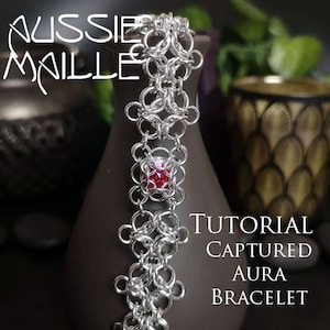 May include: A silver chainmail bracelet with a red gemstone in the centre. The bracelet is made with a captured aura pattern. The text "TUTORIAL CAPTURED AURA BRACELET" is visible in the image.