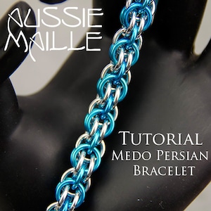 Pode incluir: Um bracelete de malha de corrente turquesa e prata, conhecido como "Medo Persian Bracelet", é mostrado em uma superfície preta. O bracelete é feito de pequenos anéis interligados. O texto "TUTORIAL MEDO PERSIAN BRACELET" é visível abaixo do bracelete.