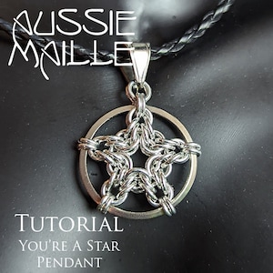 May include: A silver chainmail star pendant with a circular frame. The pendant is hanging from a black leather cord. The text "You're a Star Pendant" is written below the pendant.