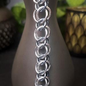 May include: A silver chainmail bracelet with a repeating pattern of interlocking rings.