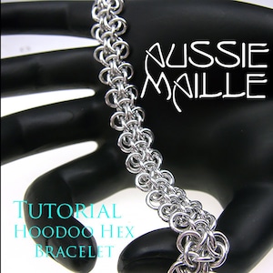 May include: A silver chainmail bracelet with a hexagonal pattern, known as "Hoodoo Hex", on a black display stand. The bracelet is labeled "Tutorial Hoodoo Hex Bracelet" and "Aussie Maille".