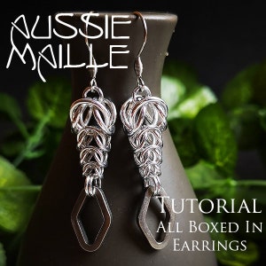 Può includere: Un paio di orecchini d'argento con un design geometrico. Gli orecchini sono realizzati in maglia a catena e hanno una forma a goccia. Gli orecchini sono appesi a un vaso marrone. Il testo "TUTORIAL ALL BOXED IN EARRINGS" è visibile nell'immagine.