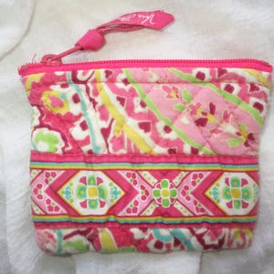 May include: A quilted fabric coin purse featuring a vibrant pink, yellow, and light green floral and geometric pattern. The pouch has a pink zipper closure with a matching fabric pull tab that displays the brand name Vera Bradley in white text.