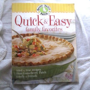 May include: A cookbook titled "Quick & Easy family favorites" by Gooseberry Patch. The cover shows a photo of a savoury pie with a golden crust, served from a green dish. The book's title is in large red letters.
