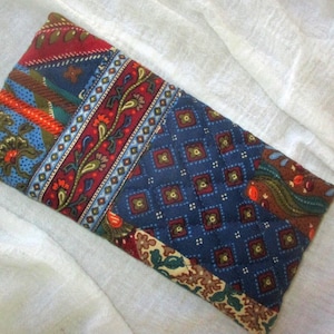 May include: Rectangular fabric pouch with a patchwork design. The pouch features a combination of patterns in red, blue, green, and orange. The patterns include floral, paisley, and geometric shapes. The pouch is likely used for storing small items.