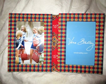 May include: Open photo album with a red, blue, and yellow plaid pattern. The left side displays a photo of cheerleaders. The right side has a blue card with "Vera Bradley" and "verabradley.com" printed on it.