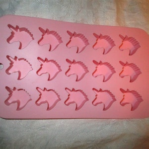May include: A pink silicone mold with fifteen unicorn head-shaped cavities. The mold has a rectangular shape with a handle hole on one side. The unicorn heads are detailed with a horn, mane, and facial features.