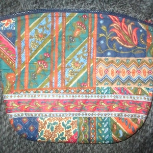 May include: A quilted cosmetic bag with a patchwork design. The bag features a variety of colorful fabric patterns, including floral and geometric motifs in shades of teal, orange, red, and blue. The top edge is trimmed with a dark blue zipper.