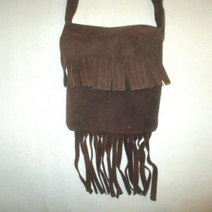 May include: A brown suede shoulder bag with a long strap. The bag features a fringed design on the top and bottom. The bag is made of a soft, textured material.