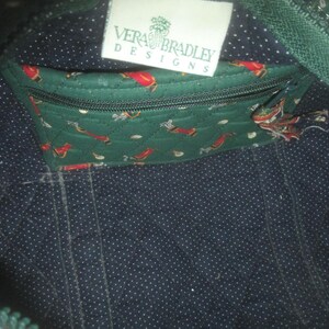 May include: The interior of a quilted bag featuring a dark blue fabric with white polka dots. A green quilted zippered pocket with a golf-themed print is attached, and a white rectangular tag reads Vera Bradley Designs in green text.