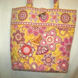 May include: A quilted tote bag with a floral pattern in shades of yellow, pink, and red. The bag features a button closure and matching handles. The floral design is repeated across the bag's surface.