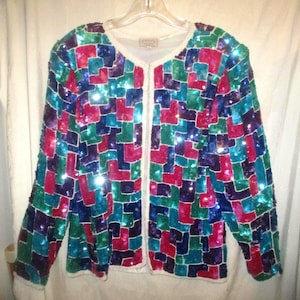May include: A colorful sequined jacket with a geometric pattern in shades of blue, green, purple, and pink. The jacket has a white trim and is hanging on a hanger.