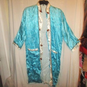 May include: A turquoise satin robe with a white satin lining and trim. The robe has a quilted texture, long sleeves, and brown buttons. The edges are trimmed with black and gold detailing. A vintage garment.