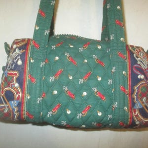 May include: A quilted green handbag featuring a repeating pattern of red golf bags and white golf balls. The side panels are dark blue with a detailed print of golf clubs, bags, and plaid accents. It includes two fabric handles and a zipper.
